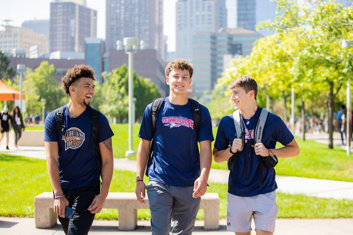 Three students standing together in front of greenery and the 丹佛 skyline.